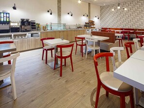 A restaurant interior with wooden flooring, red and white chairs, tables, a counter with a coffee machine, and a patterned wall. - ibis Styles Amsterdam Amstel (Amsterdam)