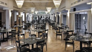 Un comedor amplio con múltiples mesas y sillas, grandes candelabros y un techo alto.