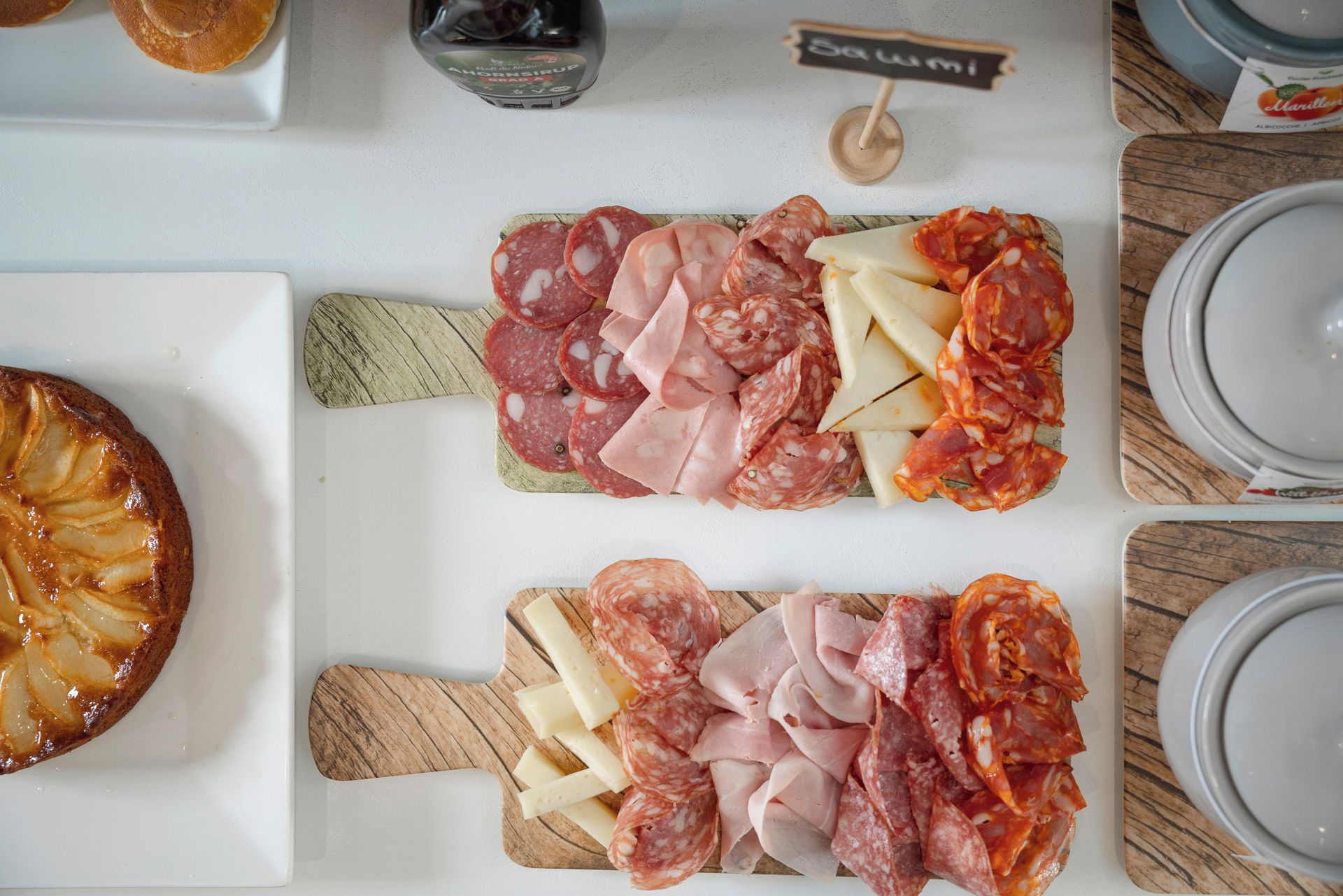 Une table sur laquelle on trouve divers aliments, notamment des charcuteries et des fromages en tranches, une miche de pain et une bouteille de sauce.