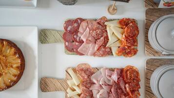 Une table sur laquelle on trouve divers aliments, notamment des charcuteries et des fromages en tranches, une miche de pain et une bouteille de sauce.