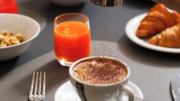 En frukostuppsättning med en kopp kaffe, ett glas apelsinjuice och croissanter på ett bord.