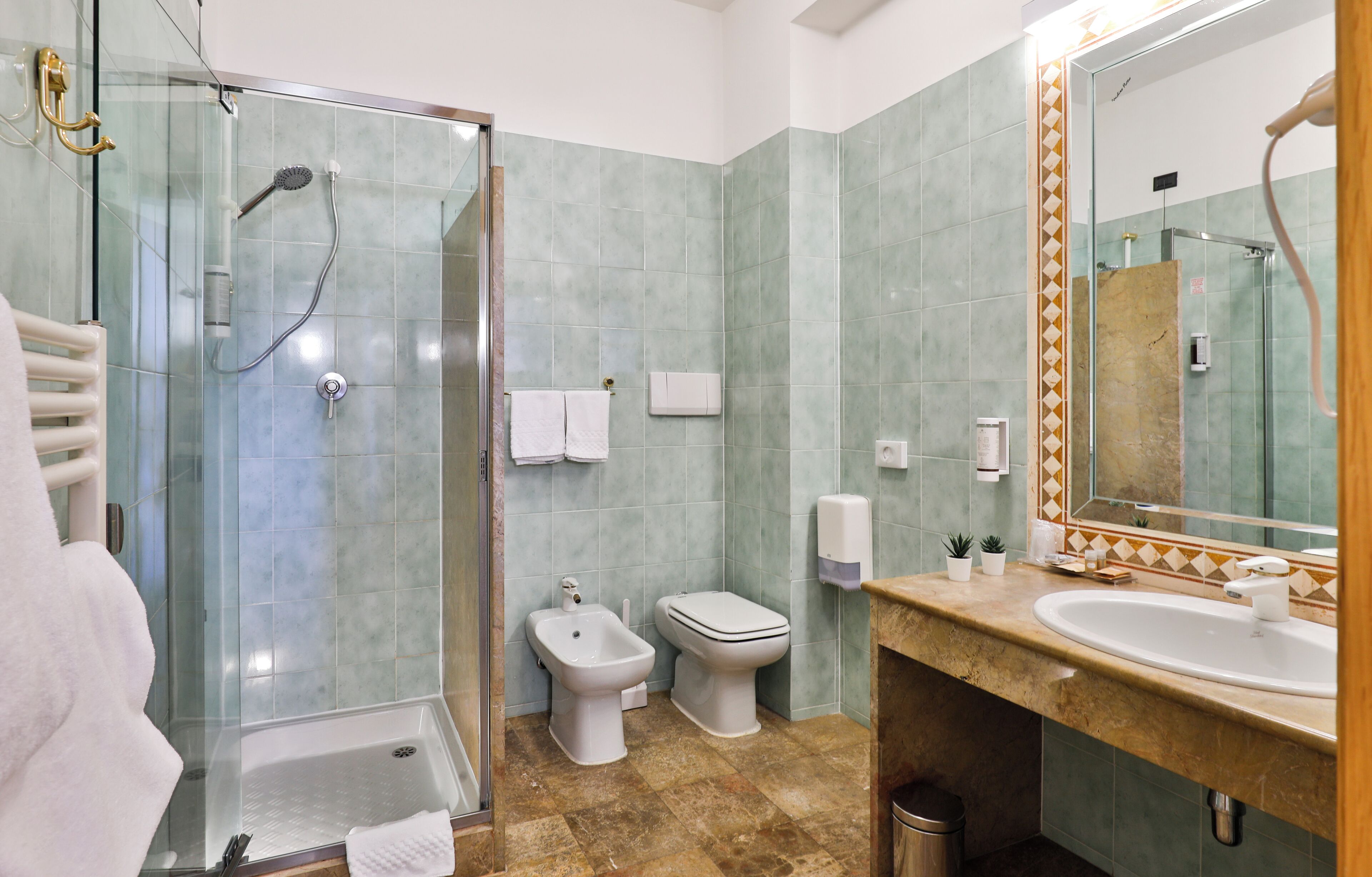 Un baño con cabina de ducha de vidrio, un bidé, un inodoro, un lavabo y un espejo con marco decorativo.