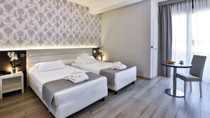 Habitación de hotel con dos camas, una mesita pequeña con una silla y un detalle decorativo en la pared.