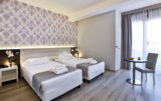 A hotel room with two beds, a small table with a chair, and a decorative wall.