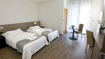A hotel room with two beds, a small round table with a chair, and a window with curtains.
