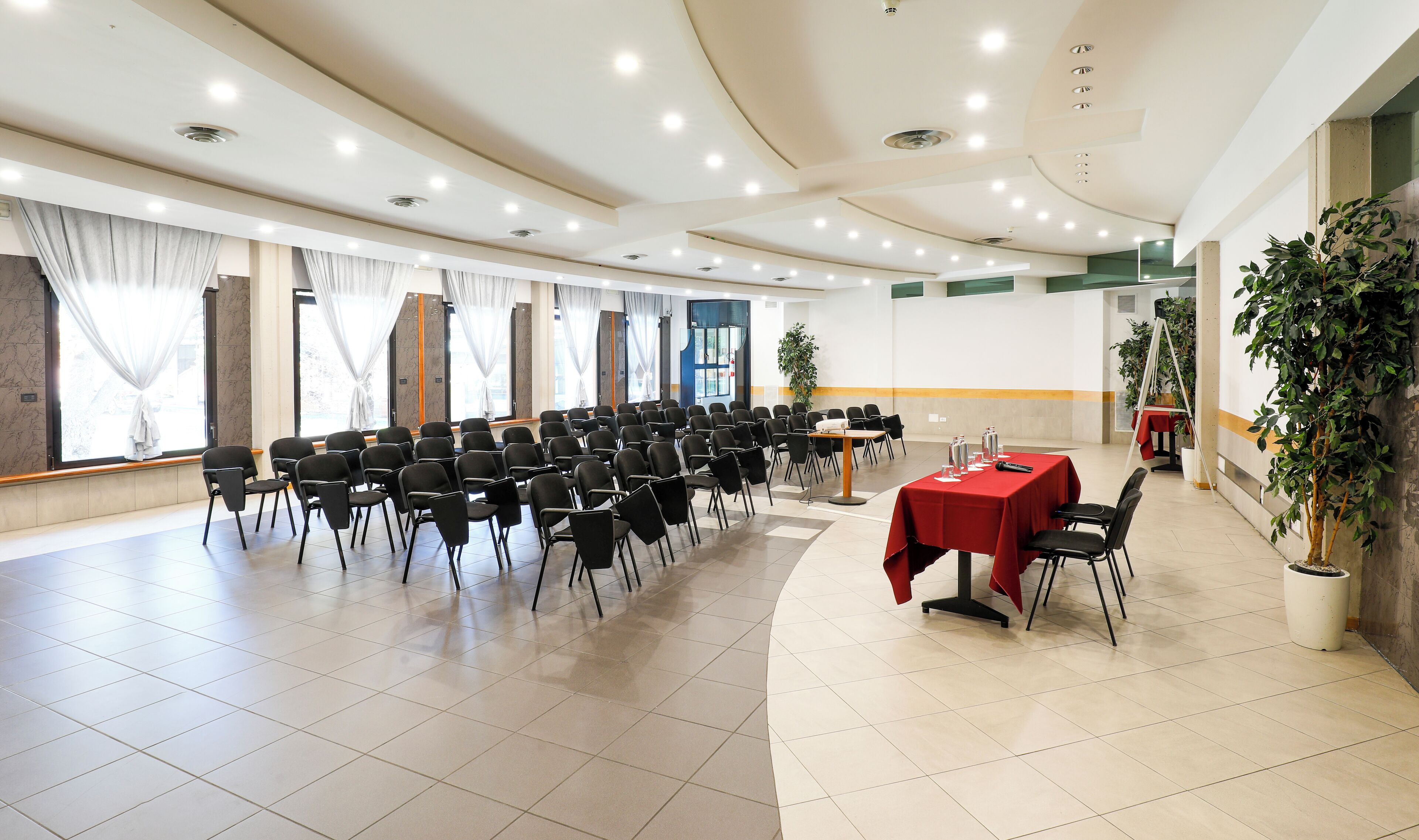A conference room with rows of chairs, a table with a red tablecloth, and a potted plant.