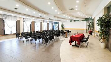 Un salón de conferencias con filas de sillas, una mesa con mantel rojo y una planta en maceta.
