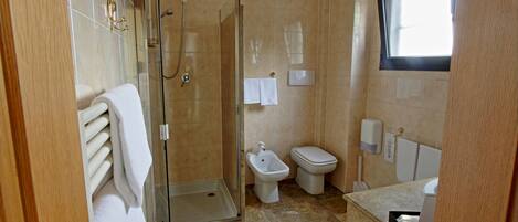 Een badkamer met een douche met glazen wand, toilet, bidet en wastafel.