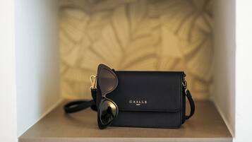 Un bolso negro con gafas de sol encima, sobre una estantería con un fondo estampado.