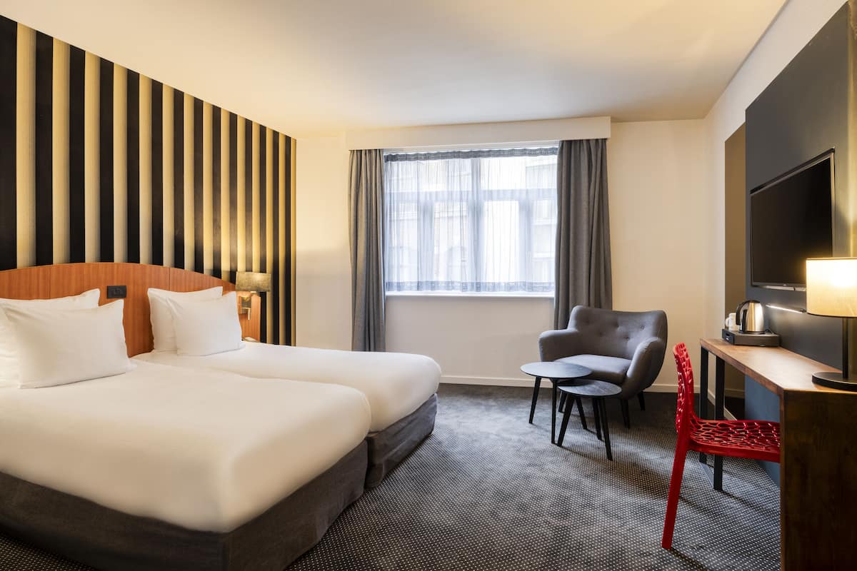 A hotel room with a large bed, a desk with a lamp, a chair, and a TV.