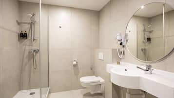A modern bathroom with a glass-enclosed shower, a white toilet, and a large mirror above the sink.