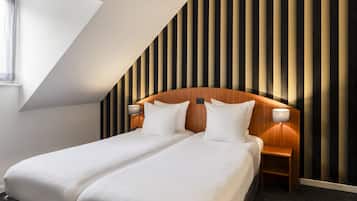 Een moderne hotelkamer met een schuin dak, een houten hoofdeinde, twee bedden met witte lakens, een nachtkastje met een lamp, en een gestreept wandontwerp.