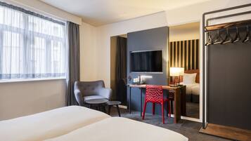Ein Hotelzimmer mit zwei Betten, einem Schreibtisch, einem Stuhl, einem Fernseher und einem Spiegel.
