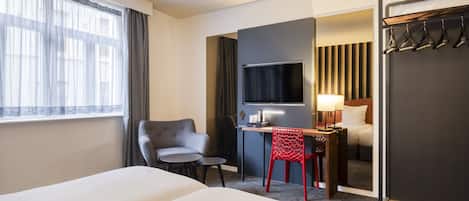 Ein Hotelzimmer mit zwei Betten, einem Schreibtisch, einem Stuhl, einem Fernseher und einem Spiegel.