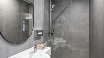 A modern bathroom with a glass-enclosed shower, a round mirror, and a white sink.
