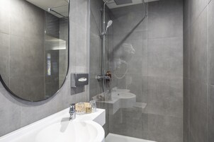 A modern bathroom with a glass-enclosed shower, a round mirror, and a white sink.