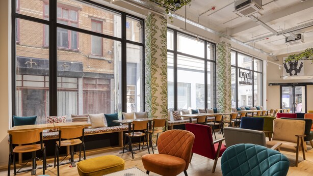 A modern interior with large windows, wooden tables, and colorful chairs. - Aris Grand-Place Hotel (Brussels)
