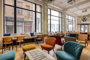 A modern interior with large windows, wooden tables, and colorful chairs. - Aris Grand-Place Hotel (Brussels)