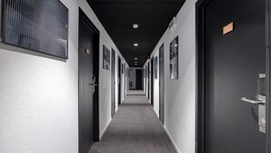 A hallway with doors on both sides, numbered signs, and a carpeted floor. - Aris Grand-Place Hotel (Brussels)