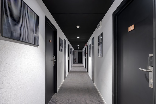 A hallway with doors on both sides, numbered signs, and a carpeted floor. - Aris Grand-Place Hotel (Brussels)