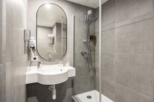 A modern bathroom with a white sink, a large mirror, and a glass-enclosed shower.
