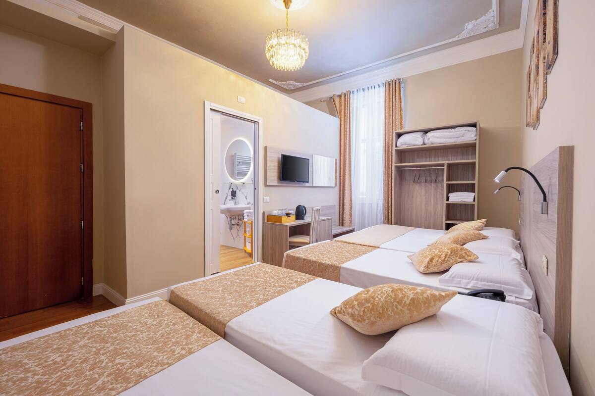 Habitación de hotel con tres camas, televisor, escritorio con silla, armario y candelabro.
