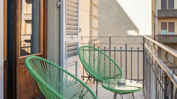 Een balkon met twee groene stoelen en een kleine tafel, een houten deur en een witte luifel.