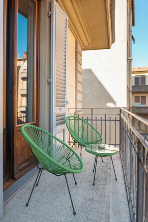 A balcony with two green chairs and a small table, a wooden door, and a white awning. - Lilium Hotel (Florence)