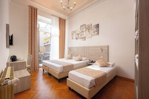 Quarto de hotel com duas camas, uma mesa com chaleira, uma cadeira e vista para um edifício.