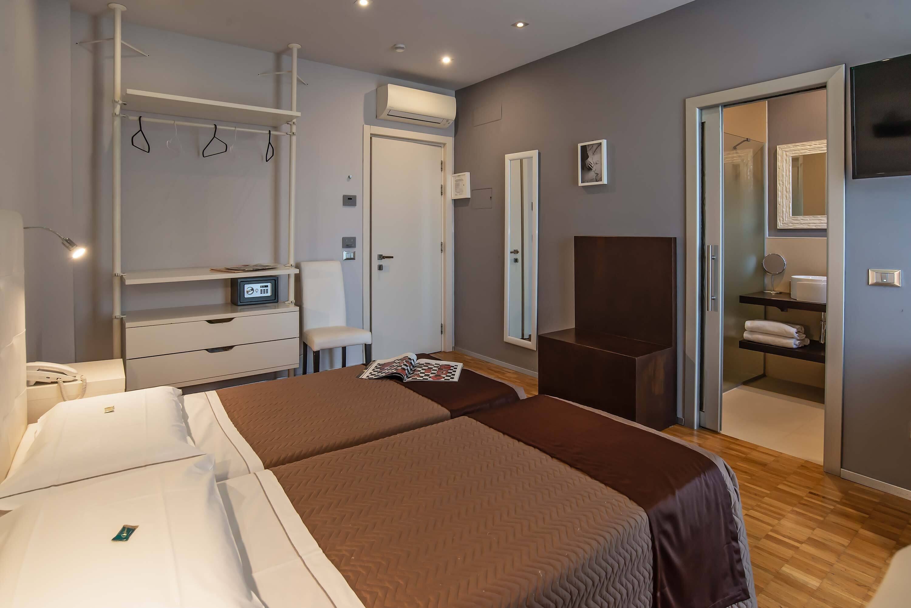 A hotel room with two beds, a wardrobe, a desk, a chair, a mirror, and a TV.