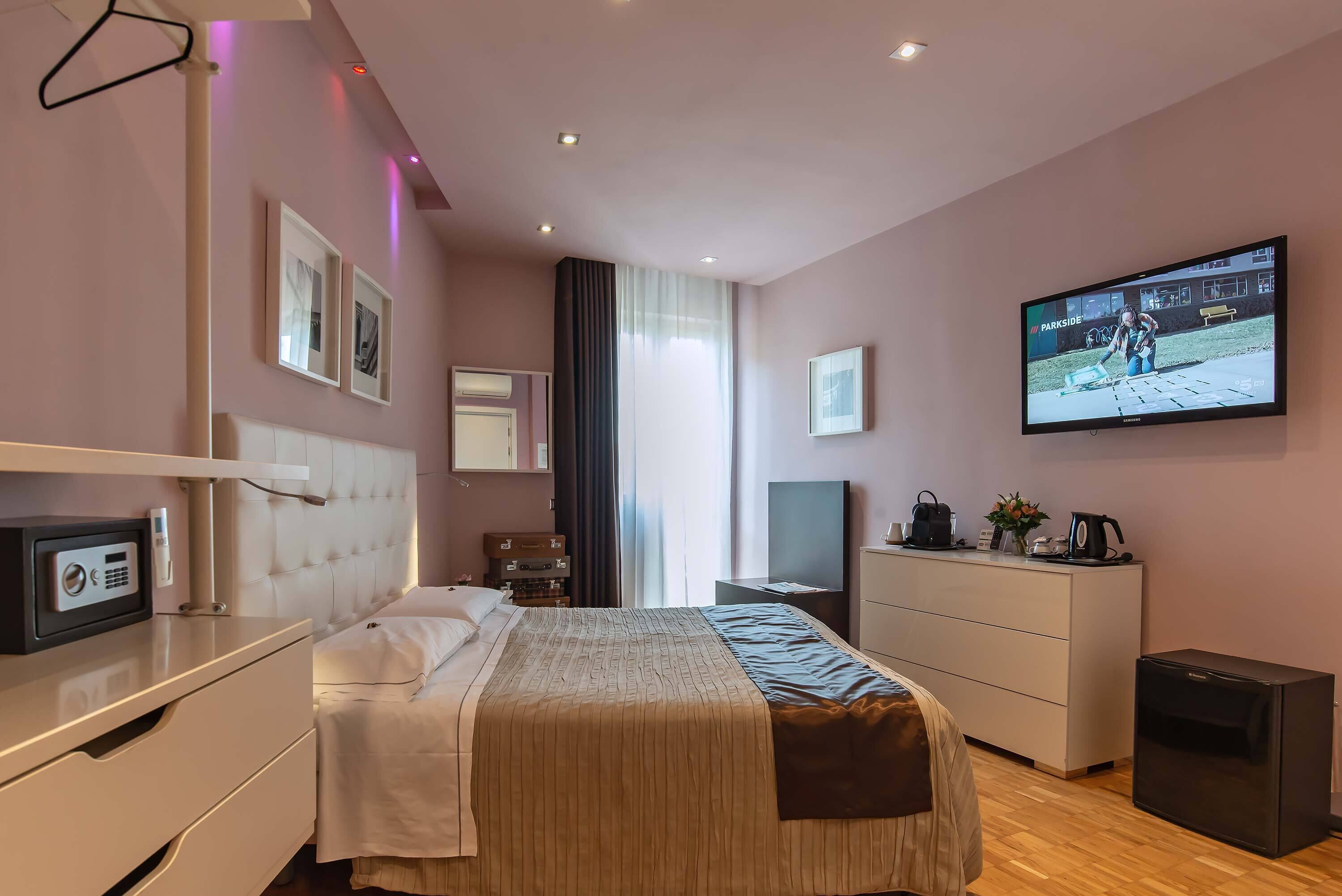 A modern hotel room with a bed, bedside table, TV, and a small refrigerator.