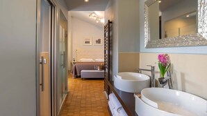 A modern bathroom with two sinks, a large mirror, and a bed in the adjacent room. - Hotel Orcagna (Florence)