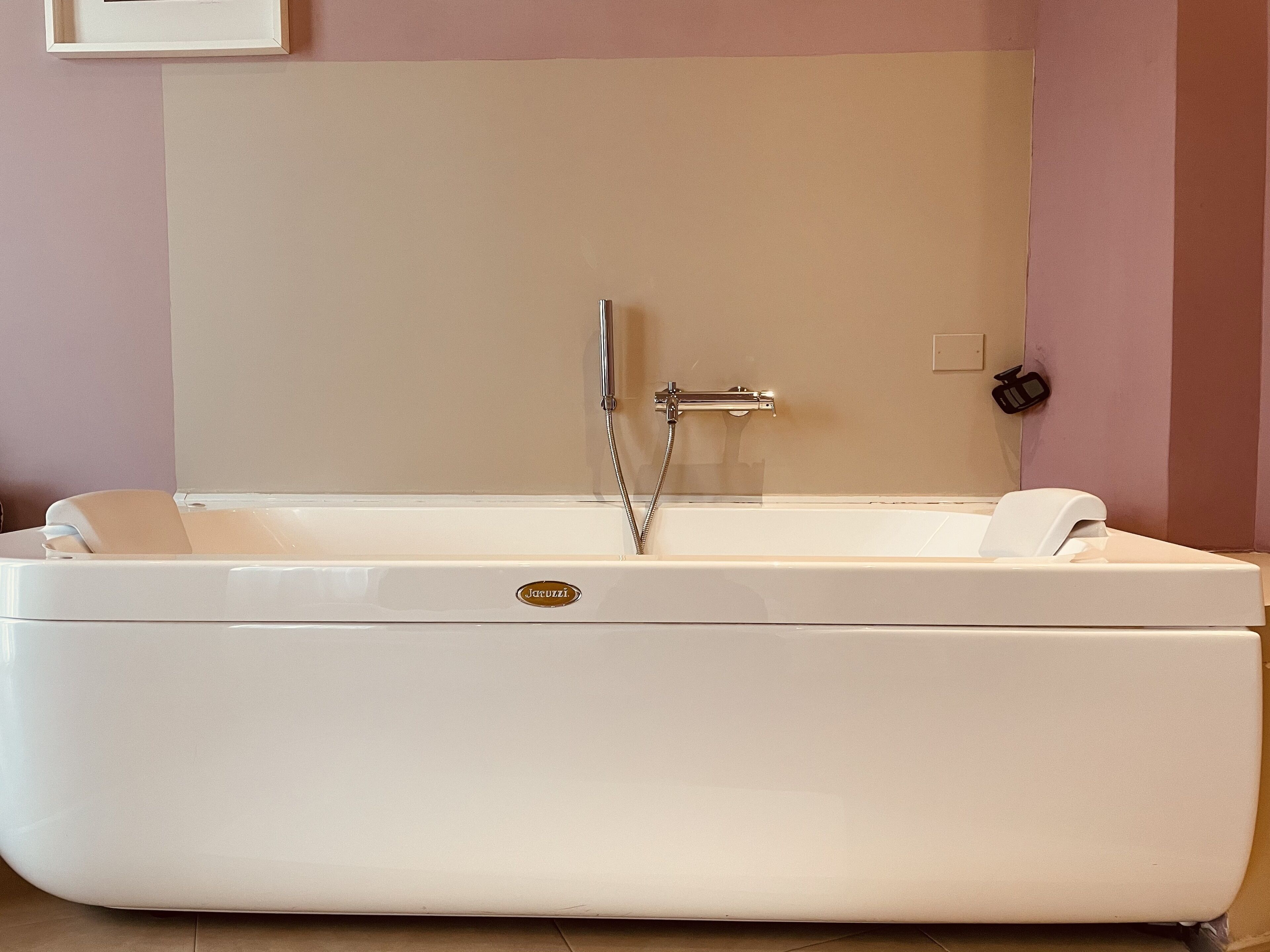 A white bathtub with a shower head and control panel, set against a wall with a light-colored panel.