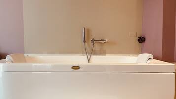 A white bathtub with a shower head and control panel, set against a wall with a light-colored panel.