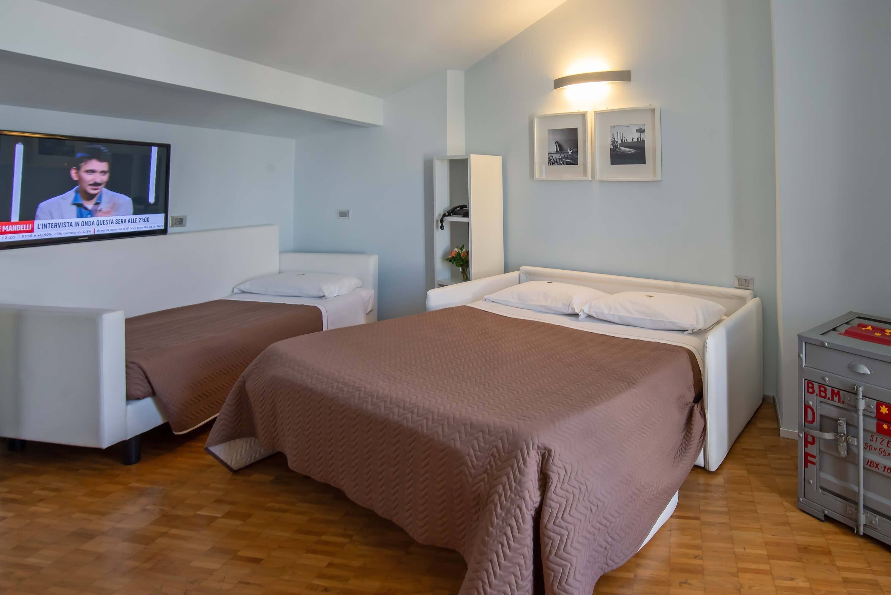 Una camera d'albergo con due letti, una TV a parete e un piccolo mobiletto.