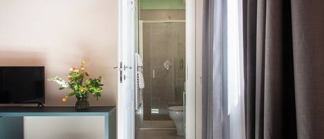 A hotel room with a television, a vase of flowers, a bedside table, a rolled-up rug, and a view into the bathroom.