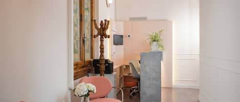 Un hall d’hôtel comprenant un comptoir d’accueil, un espace salon avec une table et des chaises, un chandelier décoratif et une plante en pot.