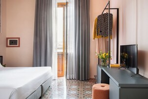 A hotel room with a bed, a desk with a computer, a mirror, and a window with curtains.