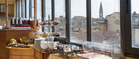 A buffet setup with various food items and a view of the cityscape through large windows.
