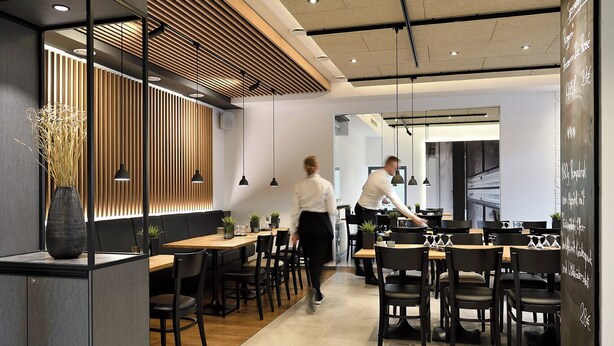 A modern restaurant interior with wooden paneling, black chairs, and a chalkboard menu. -  Werkhof Hotel (Hannover)