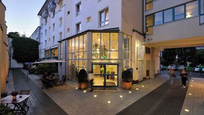 A hotel entrance with a glass facade, outdoor seating area, and a well-lit pathway. -  Werkhof Hotel (Hannover)