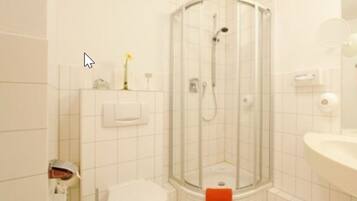 Un baño moderno con ducha envuelta en vidrio, lavamanos blanco y espejo.