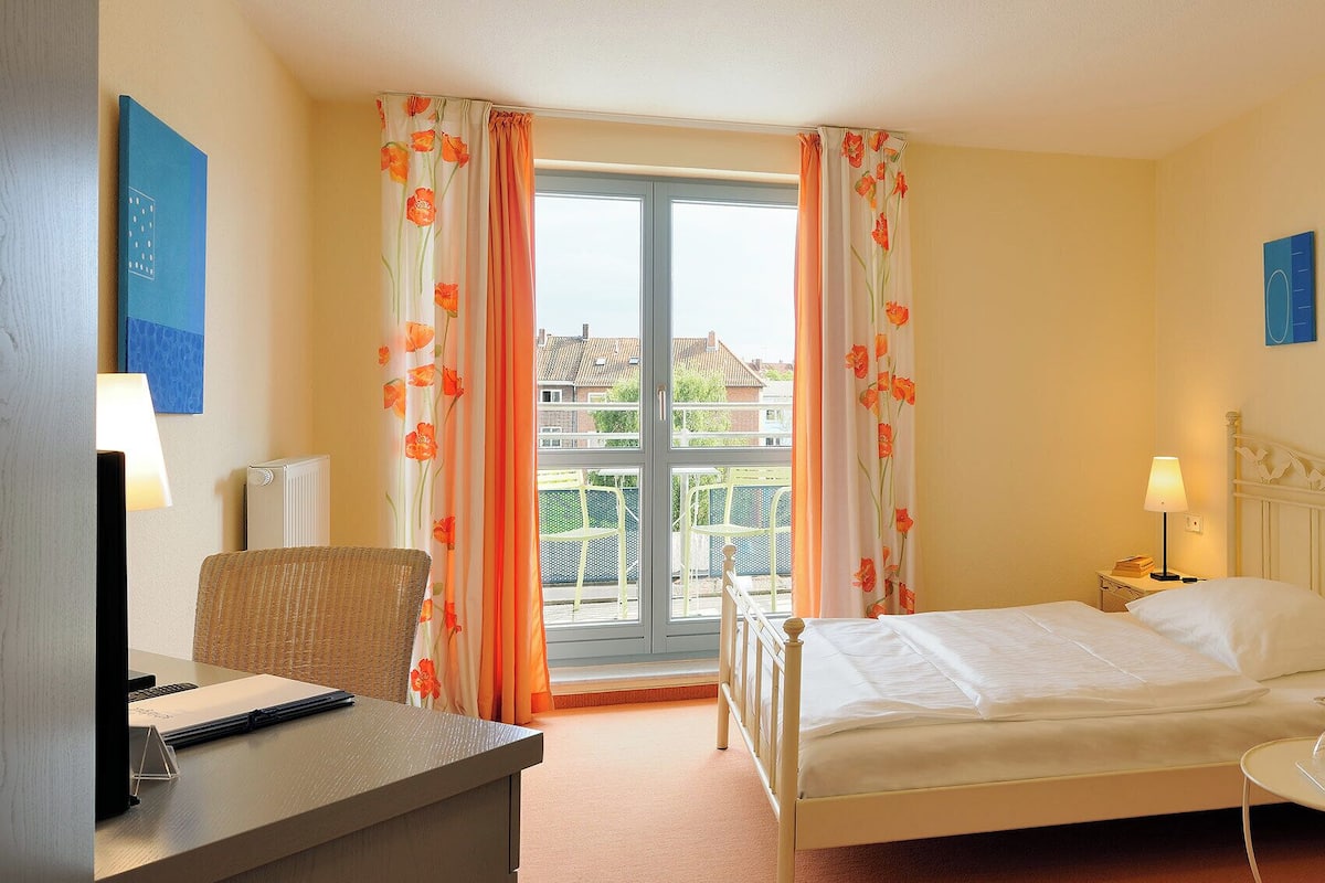 A hotel room with a bed, desk, chair, and a view of the outside.