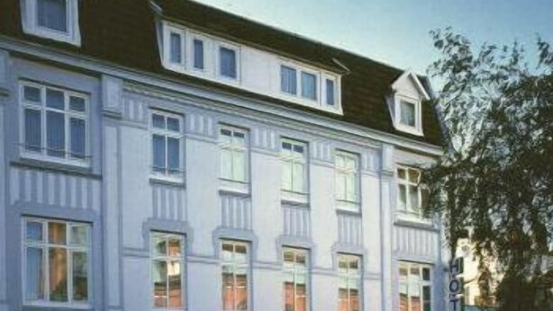 Un hôtel à plusieurs étages, de style architectural classique, caractérisé par une façade symétrique avec des fenêtres régulièrement espacées et une entrée centrale.