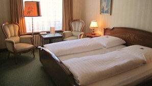 Une chambre d’hôtel avec deux lits, une chaise, une table avec une lampe et une fenêtre avec des rideaux.