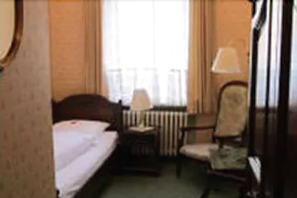 A hotel room with a bed, a chair, a nightstand, and a lamp.