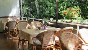 Une terrasse extérieure agrémentée de chaises et de tables en osier, entourée d’une végétation luxuriante et de fleurs.