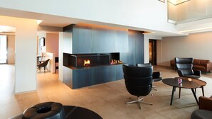A modern lobby with a fireplace, leather seating, and a dining area. - Fosshotel Husavik (Husavik)