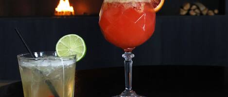 Two cocktails on a table with a fireplace in the background.