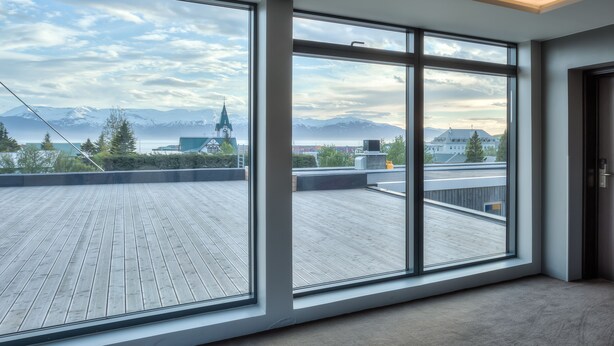 A modern room with large windows offering a view of a wooden deck and distant mountains. - Fosshotel Husavik (Husavik)